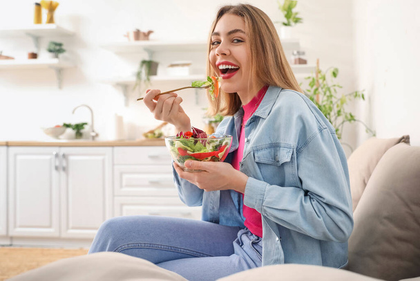Fiatal nő eszik zöldség saláta kanapén otthon - Fotó, kép