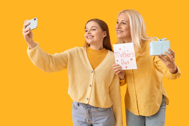 Молодая женщина и ее мать с подарком делает селфи на оранжевом фоне - Фото, изображение
