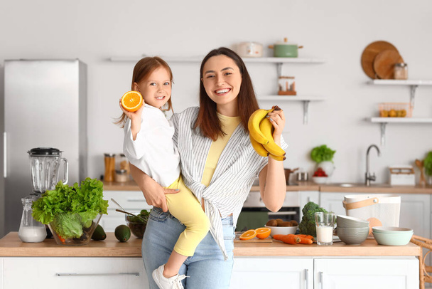 彼女の母親とキッチンで健康的なフルーツを持つ小さな女の子 - 写真・画像