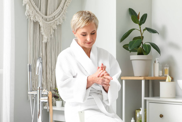 Femme mature appliquant la crème pour les mains dans la salle de bain - Photo, image
