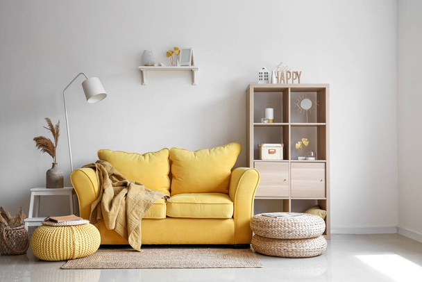 Интерьер светлой гостиной со стильным желтым диваном и мягкими пуфиками - Фото, изображение