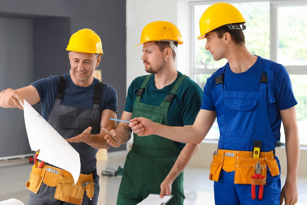 Equipo de constructores masculinos trabajando con el plan de la casa en la habitación - Foto, Imagen