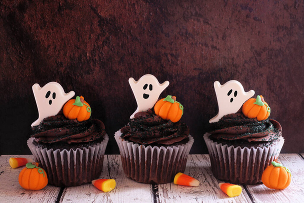 Gruselige Halloween-Schokoladen-Cupcakes mit Geistern und Kürbissen in einer Reihe vor dunklem Holzhintergrund - Foto, Bild