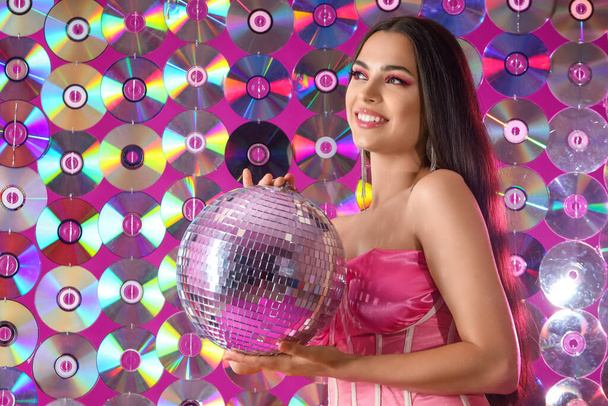 Stylish young woman with disco ball against compact disks - Foto, Bild