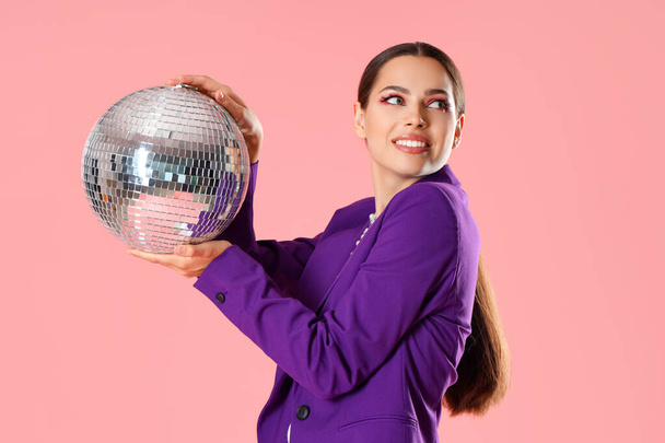 Стильна молода жінка з диско-кулькою на рожевому фоні - Фото, зображення