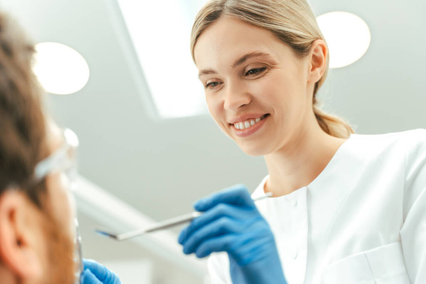 Дантист осматривает пациента в современной стоматологической клинике. Лечение зубов, здравоохранение, гигиена полости рта  - Фото, изображение