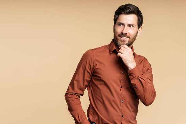 Smiling bearded middle aged businessman, manager looking away while posing isolated on beige background. Successful business concept  - Photo, Image