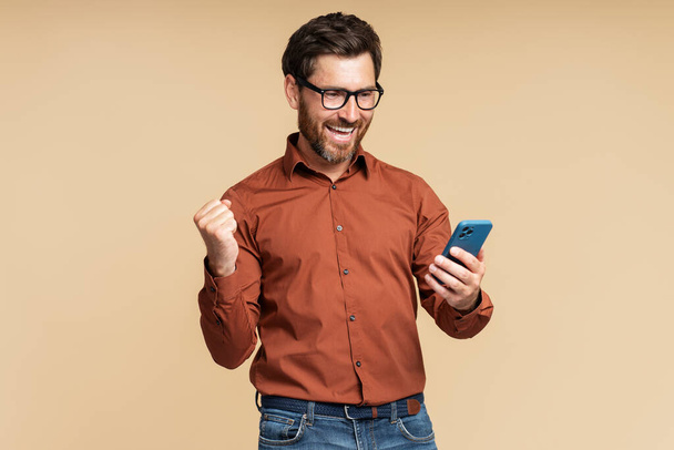 Przepełniony radością człowiek trzyma zakupy smartfona w sieci ze sprzedażą odizolowaną na tle. Emocjonalny hipster za pomocą aplikacji mobilnej, zakłady sportowe, wygrać pieniądze koncepcja uroczystości. Szczęśliwy freelancer otrzymać płatność - Zdjęcie, obraz