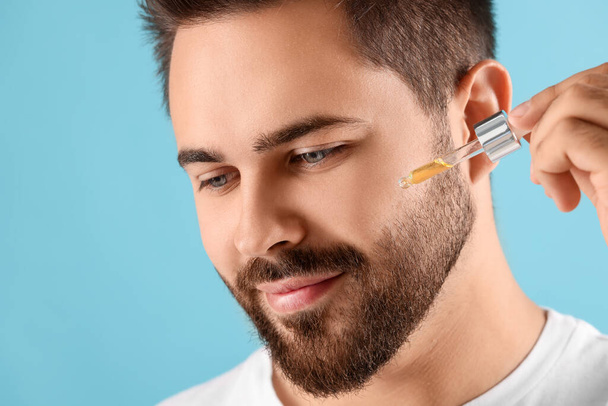 Handsome man applying cosmetic serum onto face on light blue background, closeup - Foto, imagen