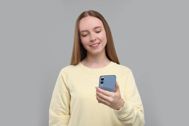 Happy young woman using smartphone on light grey background - Photo, Image