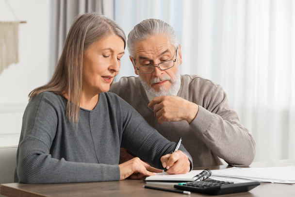 Elderly couple with papers discussing pension plan at wooden table indoors - Photo, Image