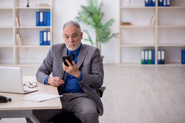 Старий співробітник розмовляє по телефону в офісі - Фото, зображення