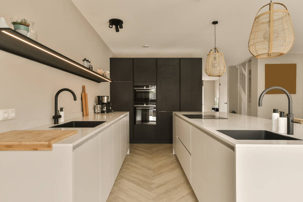 Modern bir mutfak, siyah beyaz dolaplar, ahşap döşemeler ve odanın ortasında bir ada bankı. - Fotoğraf, Görsel