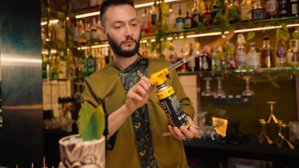 un barista in un bar o ristorante decora un cocktail alcolico appena preparato con pinze - Filmati, video
