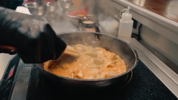 primo piano di uno chef in una cucina professionale ristorante aggiungendo salsa alla padella al curry mescolando il piatto - Filmati, video