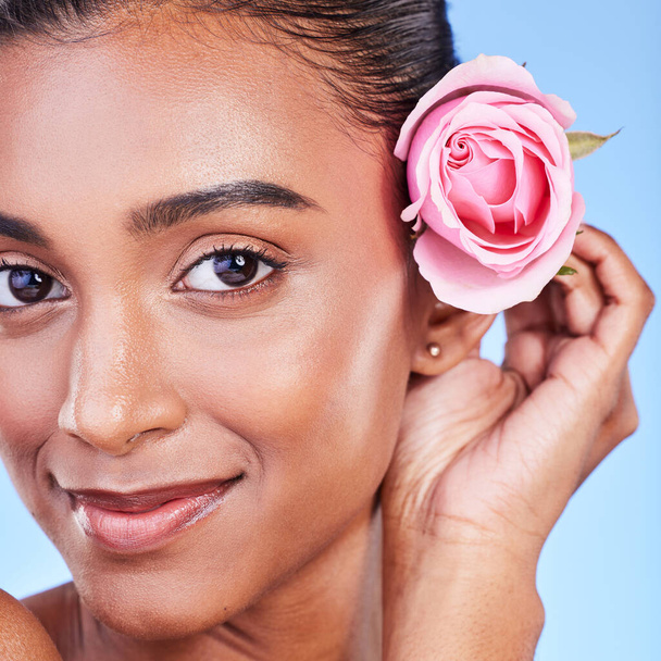 Rose, portrait and skincare of woman in studio for eco cosmetics, natural glow and aesthetic on blue background. Face, happy indian model and flowers for beauty, sustainability or floral dermatology. - Foto, afbeelding