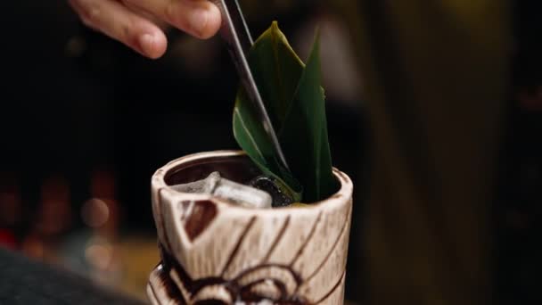 бармен в баре или ресторане украшает свежеприготовленный алкогольный коктейль выкладывает декор щипцами - Кадры, видео