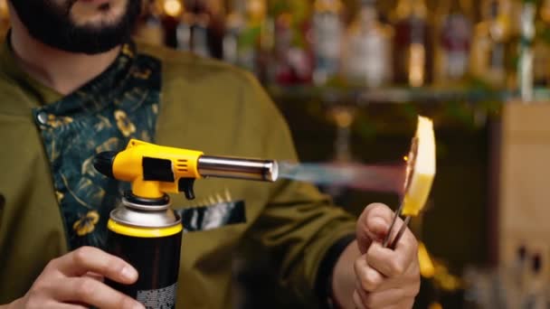 un barista in un bar o ristorante brucia un pezzo di ananas con il fuoco decorare un cocktail alcolico - Filmati, video