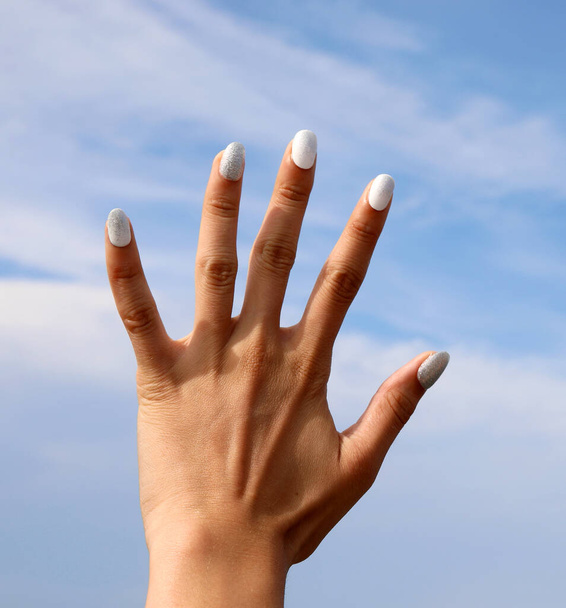 Mooie hand van het meisje met kleurrijke nagellak op nagels en lucht achtergrond - Foto, afbeelding