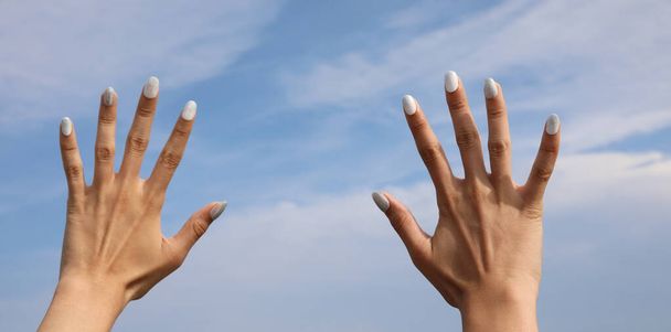 дві руки дівчини з лаком на нігтях і небом на фоні - Фото, зображення