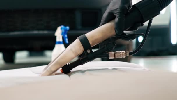 Крупним планом працівник автомийки використовує пилосос для очищення сидінь білого автомобіля в процесі розриву - Кадри, відео