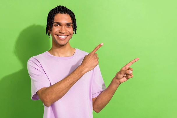 Portrait of attractive young guy stylish hairstyle directing index fingers empty space ad adv ads isolated green color background. - Foto, Imagem