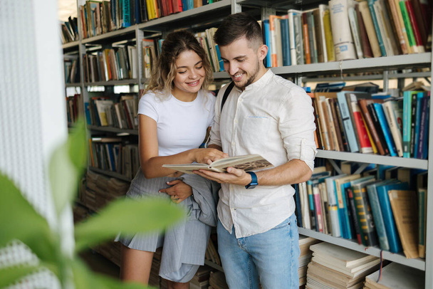 Przystojny mężczyzna i atrakcyjna kobieta szukają książki w bibliotece uniwersyteckiej. Kobieta pokazuje coś koledze z klasy w książce. Wysokiej jakości zdjęcie - Zdjęcie, obraz