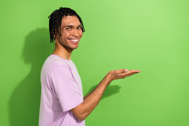 Profile photo of positive young man beaming smile hands hold demonstrate empty space isolated on green color background. - Zdjęcie, obraz