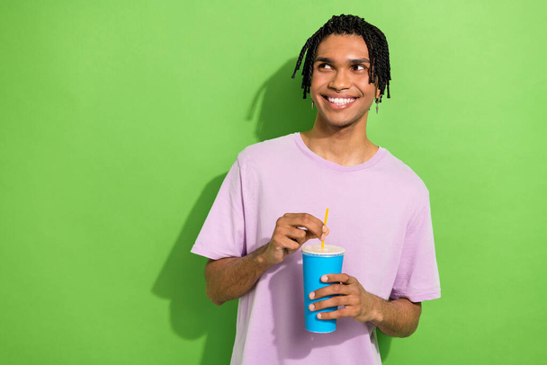 Photo of minded creative young man hold soda drink cup look empty space imagine isolated on green color background. - Фото, зображення