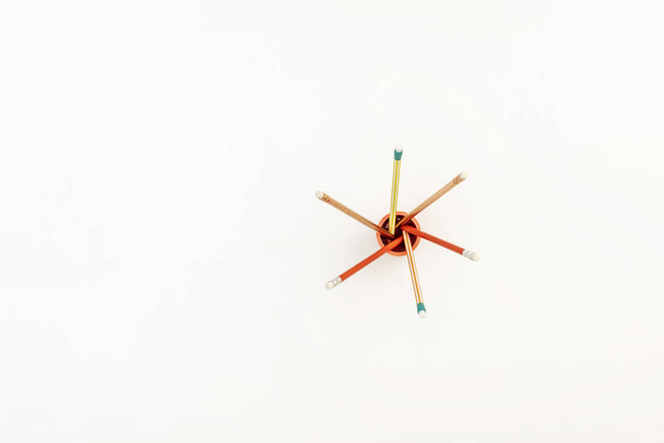 Маленькая оранжевая чаша с цветными карандашами, образующими звезду на гладкой белой поверхности - Фото, изображение