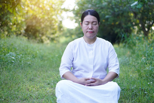 Aasialainen nainen buddhalainen pukeutuu valkoiseen pukuun, meditaatio istuu rauhallisessa metsässä. Konsepti, uskon kulttuuri. Uskonnollista toimintaa. Mielenhallinnan rauha. Tee pitoisuus.         - Valokuva, kuva
