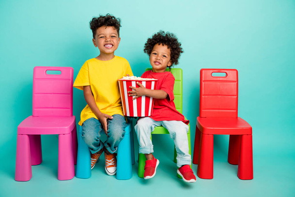 Full length photo of charming schoolboys sit chairs popcorn watch cartoon dressed stylish garment isolated on cyan color background. - Фото, изображение