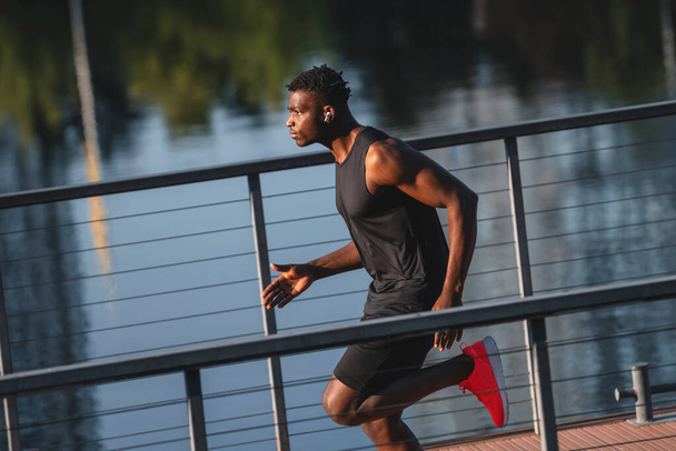Concentrated young African man in sportswear running by the riverbank - 写真・画像