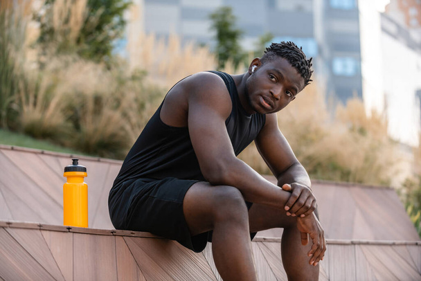Handsome African man in sportswear resting after sport training outdoors - 写真・画像