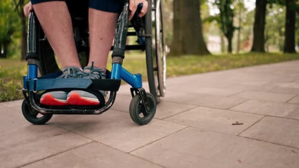 Primer plano de las piernas del hombre en silla de ruedas en el parque de la ciudad movilidad concepto de salud estilo de vida activo - Metraje, vídeo