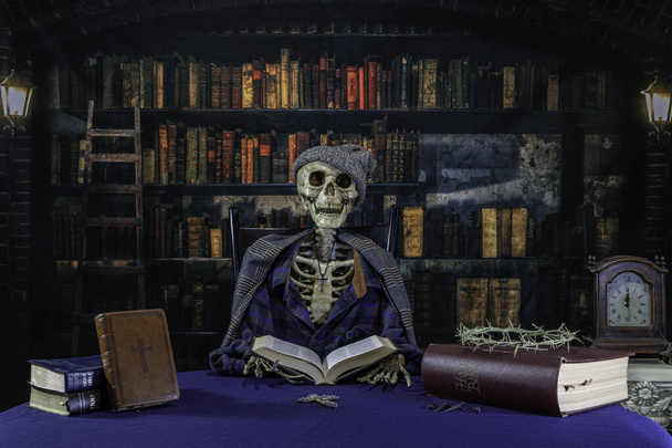 squelette portant chapeau et écharpe lecture de la bible dans une vieille bibliothèque avec des épines croisées et des clous de tête de rose - Photo, image