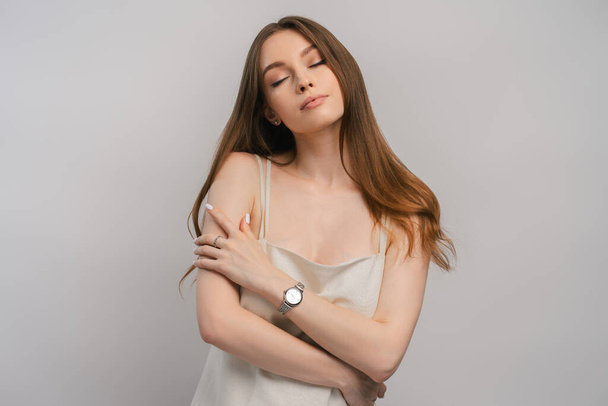 Portrét roztomilé ženy objímající se s hodinkami na ruce izolované na šedém pozadí. Krásná fenka v krásné noční košili pózuje ve studiu se zavřenýma očima. ? oncept sexuality - Fotografie, Obrázek