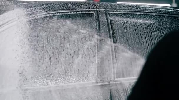 close-up masculino carro lavagem empregado aplica detergente lavagem de carro para um carro de luxo preto usando pistola de pulverização na caixa de lavagem de carro - Filmagem, Vídeo