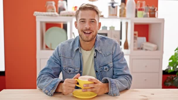 Молодий кавказький чоловік п'є каву, сидячи на столі, виступаючи в їдальні - Кадри, відео