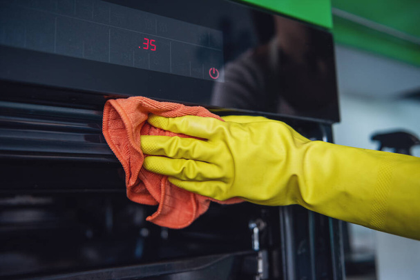 Cropped image of beautiful young woman using a duster while cleaning oven in kitchen - Photo, Image