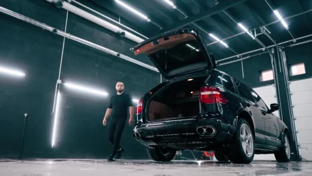 Zaměstnanec myčky stojí u otevřeného kufru černého luxusního auta v umývárně aut - Záběry, video