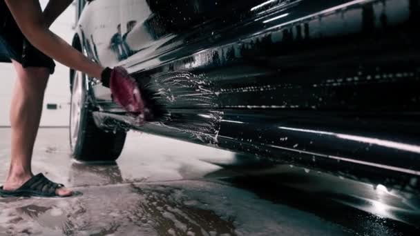 Gros plan d'un employé de lavage de voiture utilisant un chiffon en microfibre pour laver une voiture de luxe noire avec un shampooing de lavage de voiture - Séquence, vidéo