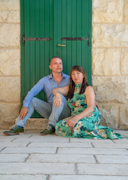 Portrait of a beautiful middle age couple in front of a green wooden gate. The man looks away and the woman looks at the camera.  - Photo, Image