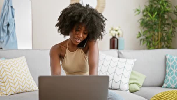 Afrikaans amerikaanse vrouw praten op smartphone met behulp van laptop het maken van notities thuis - Video
