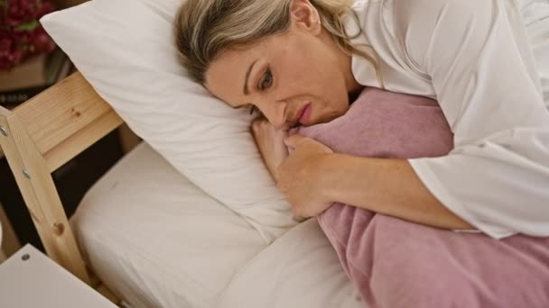 Junge blonde Frau liegt mit traurigem Gesichtsausdruck im Bett und weint im Schlafzimmer - Filmmaterial, Video