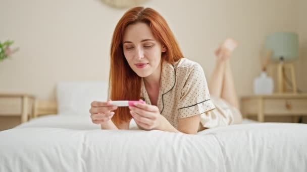 Mladý ryšavý žena úsměv jistý držení těhotenský test v ložnici - Záběry, video