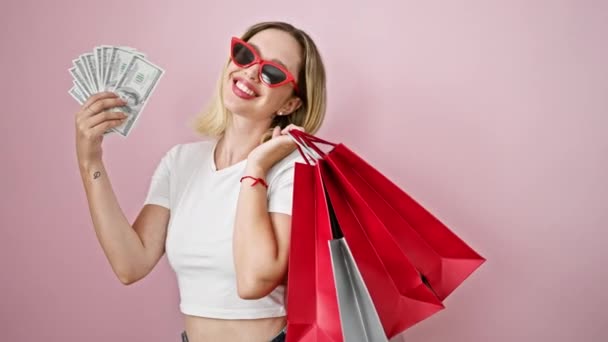Jeune femme blonde client tenant des sacs à provisions et des dollars sur fond rose isolé - Séquence, vidéo