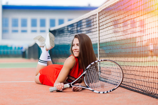 Όμορφη γυναίκα τενίστρια στο γήπεδο τένις με κόκκινο φόρεμα. - Φωτογραφία, εικόνα