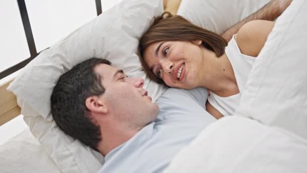 Piękna para uśmiechnięta pewna siebie leżąca razem na łóżku i mówiąca w sypialni - Materiał filmowy, wideo