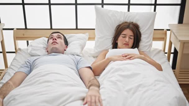 Hermosa pareja acostada en la cama cubriendo oídos para el ruido en el dormitorio - Imágenes, Vídeo